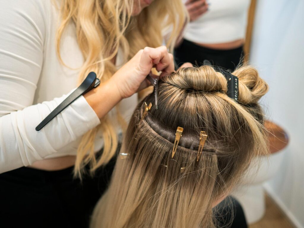 Professional hair stylist installing weft hair extensions for a client at Coastal Blondes Mooloolaba.